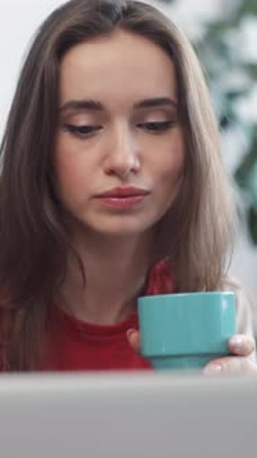 Woman Drinks Coffee, Looks at Laptop at Home