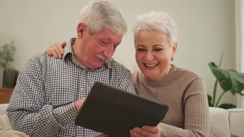 Smiling Senior Couple Uses Tablet Device at Home