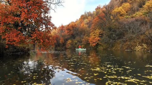 Fisherman Kayaking on Calm River Surrounded By Colorful Autumn Trees