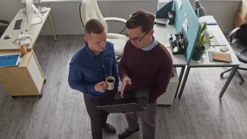 Man Holding Laptop Talking to Colleague during Work Discussion at Office