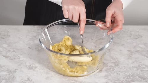 Smashing Riped Bananas in a Glass Mixing Bowl to Prepare Coconut Banana Pancakes