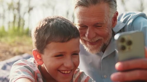 Grandfather and Grandson Use Smartphone Together Outside
