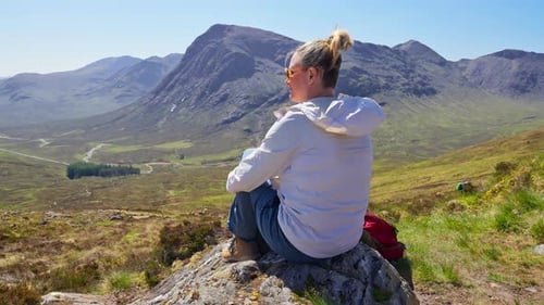 4K Wanderfrau sitzt und entspannt sich am Aussichtspunkt über eine atemberaubende Berglandschaft, Schottland