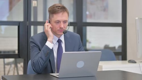 Mature Adult Businessman with Headset Working on Laptop