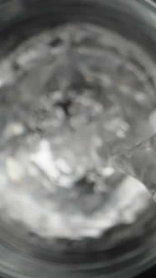 I pour clean water from a glass bottle, the camera is inside the glass, top view. Slider Dolly