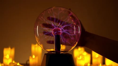 Hand touches plasma ball surrounded by candles