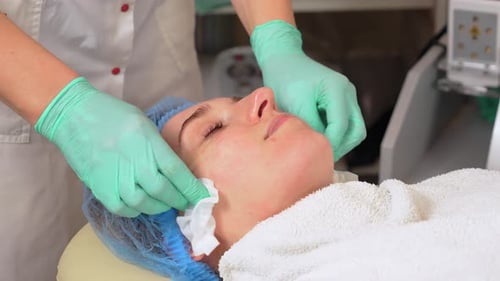 Close Up Cosmetician in Medical Gloves Removes Remains of Cosmetic Face Mask From Female Face with