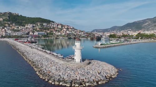 Aerial Video of a Coastal White Lighthouse With a Flag Surrounded By Blue Waters and a Scenic