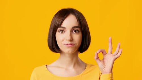 Enthusiastic Woman Gestures Ok Sign on Yellow Background