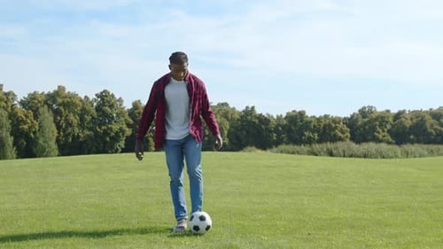 Geschickter attraktiver afrikanischer Mann, der Fußball auf dem Bein auf dem Rasen im Park hüpft