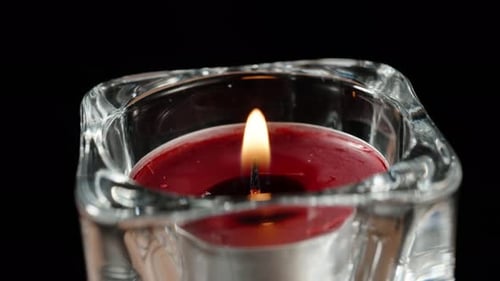 Eine rote Kerze in einem Glaskerzenhalter dreht sich und brennt auf schwarzem Hintergrund, Nahaufnahme.
