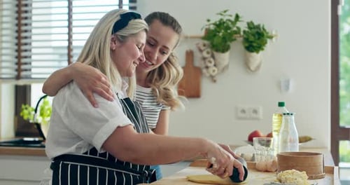 Happy Young Daughter Hugging Edlerly Mother While Middle Aged Woman Rolling Homemade Dough on Wooden