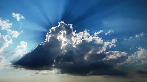 Slow drifting clouds with radiant sun beams piercing through dramatic formations in a bright blue