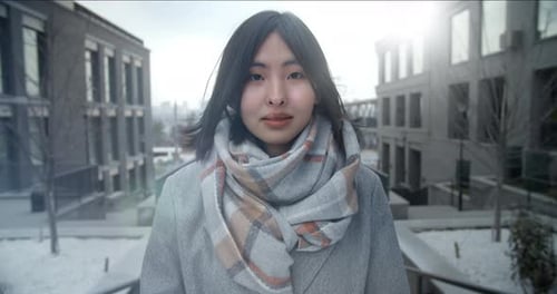 Uma jovem e bonita mulher asiática fica entre prédios comerciais e olha para a câmera