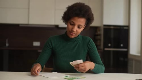 Portrait of AfricanAmerican Young Housewife Writing Financial Information on Paper Counting Counting