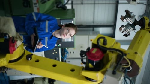 Female Engineer Inspecting Robotic Arm in Modern Factory