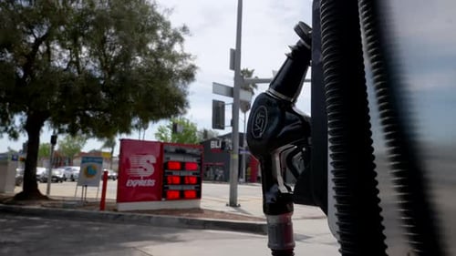 Gas Pump Handle with Gas Price Sign in Background. Low Angle Cinematic Camera Move. California.