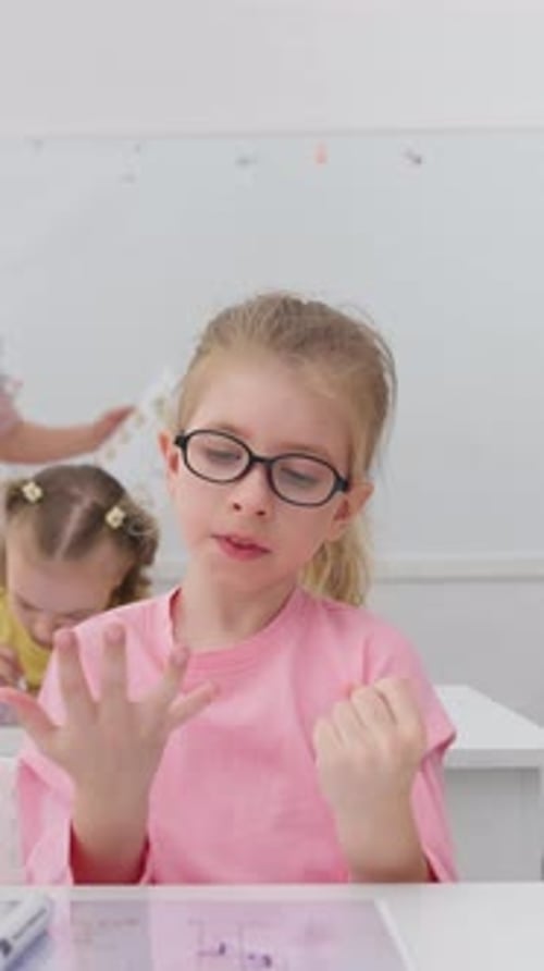 Young Schoolgirl with Glasses Counting on Her Fingers in Bright Classroom