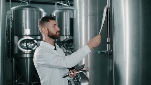 Un technologue brassicole professionnel consulte des données sur des cuves cylindroconiques destinées à la fermentation