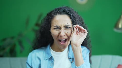 Camera view of amazed shocked young curly woman with glasses looking into camera demonstrates wow