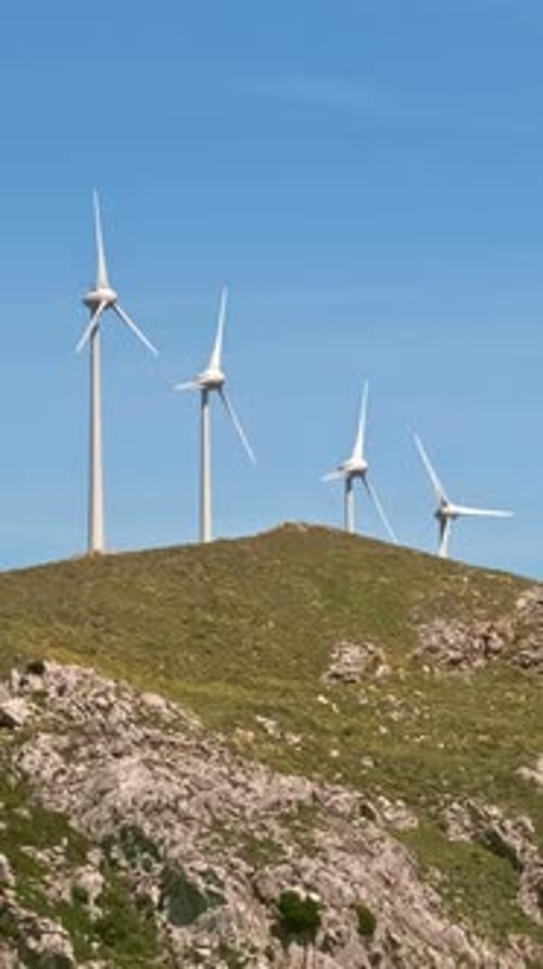 Zooming in shot of wind turbine farm in hill landscape on sunny day