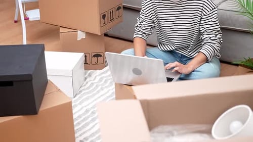 Woman Uses Laptop Surrounded by Moving Boxes