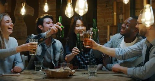 Slow motion of happy young friends having fun together drinking beer and clinking glasses in a pub