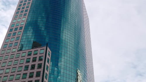 Eine wunderschöne, flüssige Fahraufnahme eines hohen blauen Wolkenkratzer-Geschäftshauses in einer Innenstadt.
T