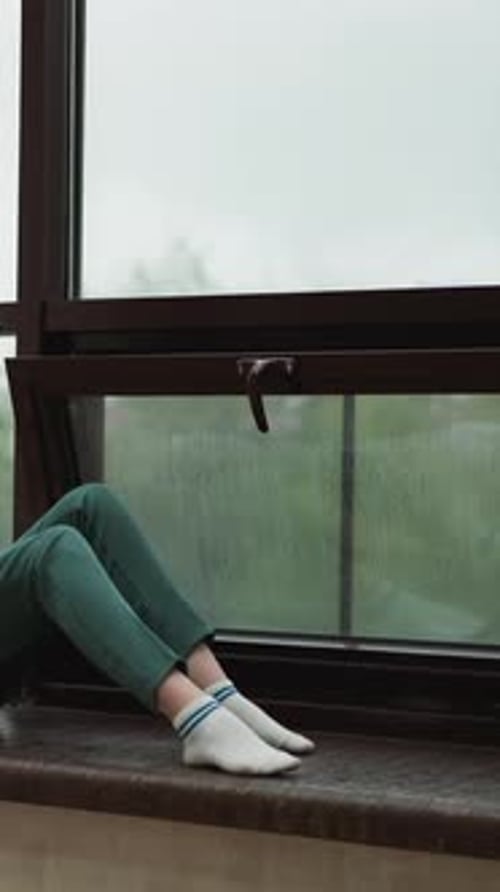 Person Sitting on Windowsill Watching Rain