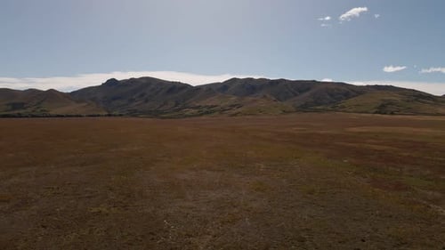 Wavy mountain range behind flat, dry plains within sunny prairie landscape. Wide angle aerial slider