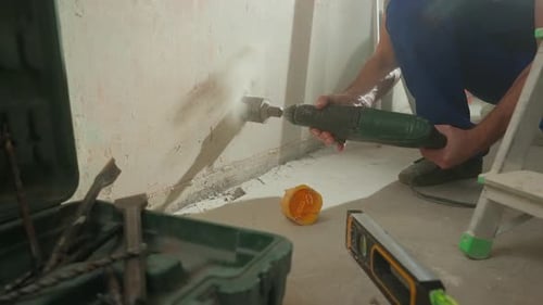 Un homme en salopette de construction bleue perce un trou rond dans un mur de béton pour y insérer une douille