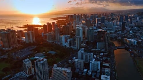 The Pacific Ocean cityscape is lit by the orange setting sun.