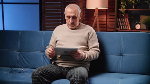 Senior Man Using Tablet on Couch Indoors