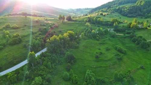 A Road Passes Hills Covered with Spruce Forests and Meadows Against a Cloudy Sky