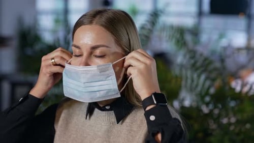 Attractive female office worker puts on mask. Lady in mask looks straight into the camera.