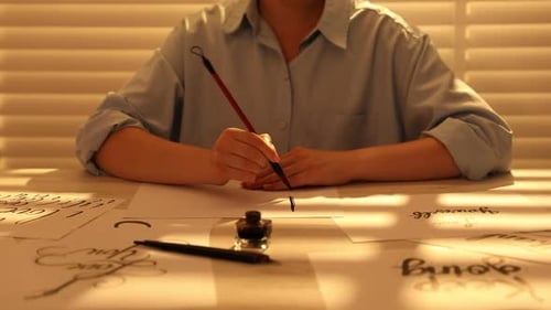 Kalligrafie. Frau mit Pinsel schreibt Wort Auf einem Blatt Papier am Tisch drinnen aufbewahren, Nahaufnahme