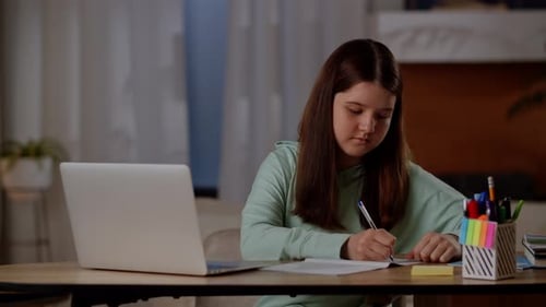 Diligent Student Writing in Notebook With Laptop