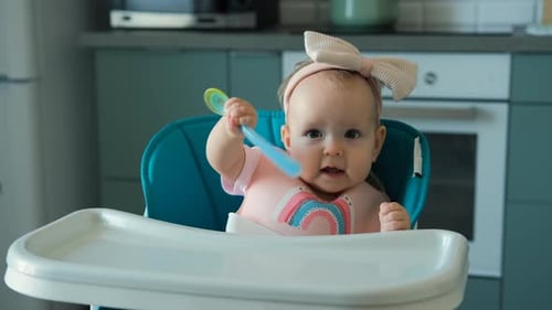 Cute Infant Plays with Spoon in High Chair