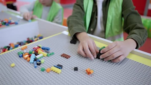 Children Playing and Building with Colorful Plastic Bricks on the Table Wearing Waistcoat in Game