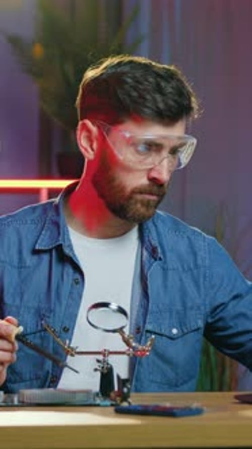 Man Soldering Electronic Component With Magnifying Glass Indoors