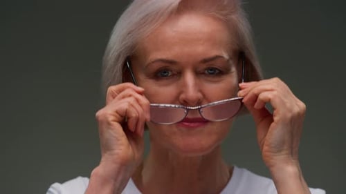 Senior Woman Puts on Glasses, Looks at Camera