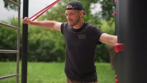 Caucasian Man Executing Intense Red Band Drill In Leafy Park Arms Extended Controlled Twists