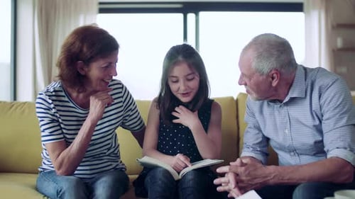 Girl Reading to Grandparents on Couch Indoors