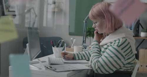 Woman Talks on Phone and Writes at Desk