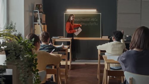 Student Raising Hand and Teacher Writing His Answer on Blackboard