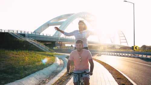Cheerful young couple having fun riding on bicycle on summer day.