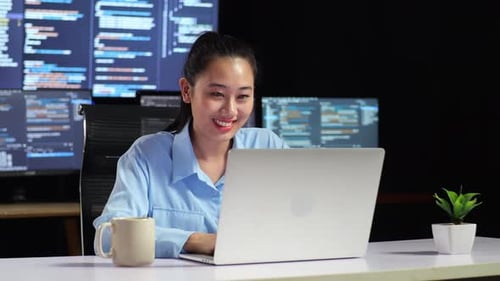 Programmeuse asiatique écrivant du code sur un ordinateur portable à l'aide de plusieurs moniteurs affichant une base de données