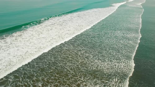 Pacific Ocean waves rolling to sandy shore viewed from above