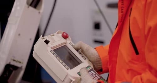 Close up of handheld robot controller with visible buttons and screen operated by gloved engineer