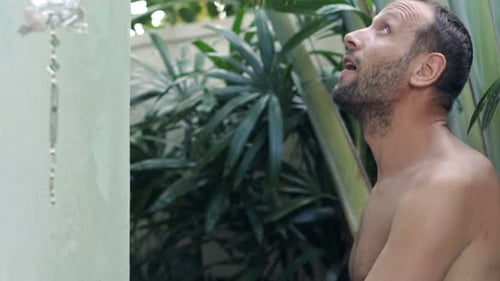 Man Enjoys Refreshing Shower Outdoors Surrounded by Lush Greenery